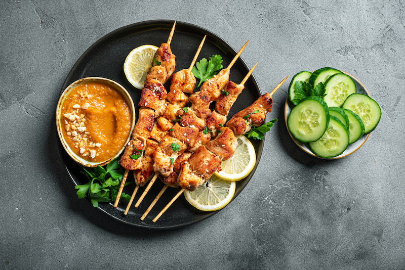 Grilled chicken satay skewers with dipping sauce and cucumber slices
