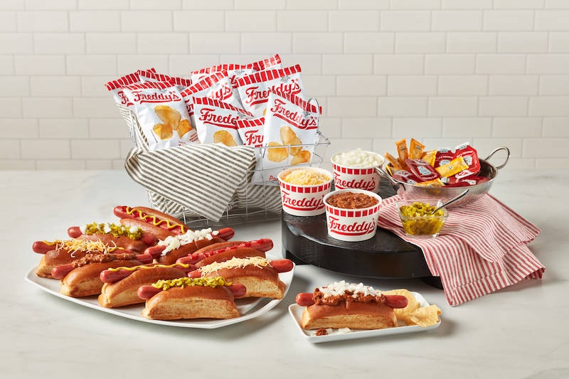 Freddy's Hot Dog Catering with assorted hot dogs with toppings, chips, cheese, and condiments on a table.