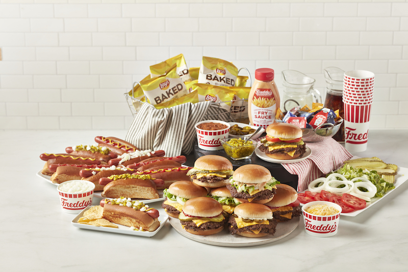 Freddy’s catering with burgers, hot dogs, chips, and toppings arranged for a large group meal.