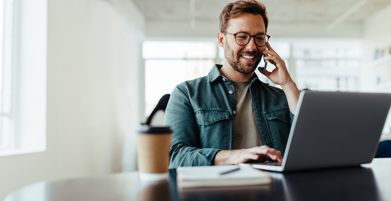 Man talking on the phone while working on a laptop at a desk