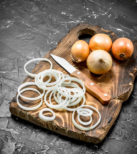 Sliced onion rings on a cutting board with whole onions