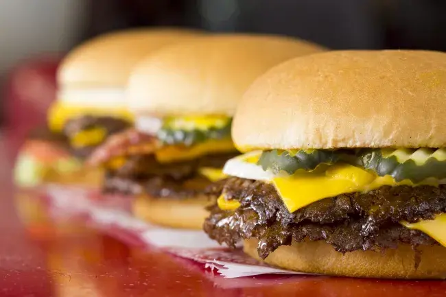 Three Freddy's Original Double Steakburgers in a line on a table.