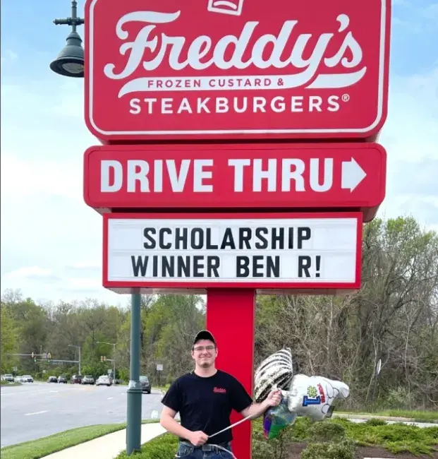 Freddy's Team member standing in front of a Freddy's sign with congratulations on their scholarship receipt.