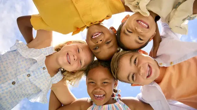Five smiling children in a circle looking down at the camera