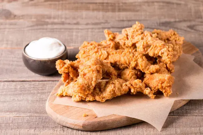 Golden fried chicken tenders on a wooden board with a side of dipping sauce