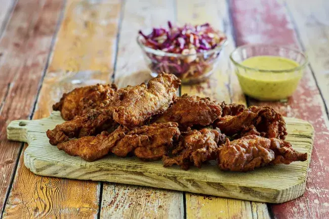 Crispy fried chicken tenders on a wooden board with coleslaw and dipping sauce