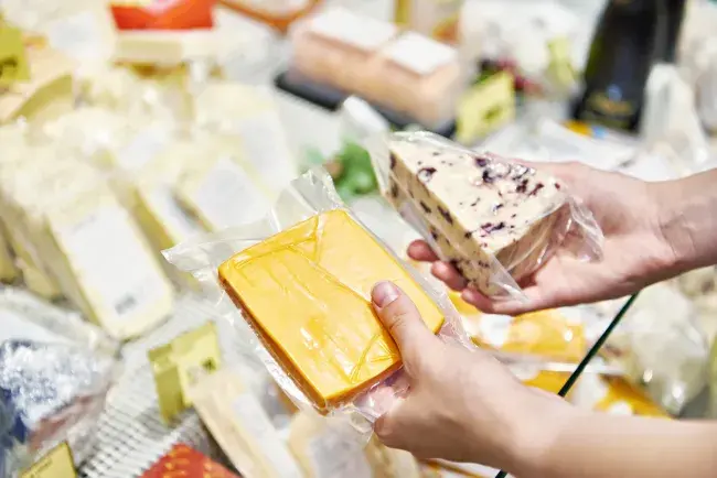 Person holding packaged cheese selections at a market display