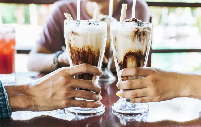 Two people clinking vanilla shakes with chocolate in tall glasses