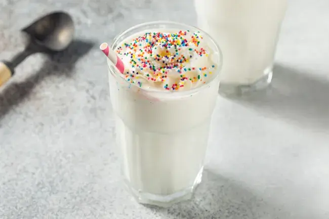 Vanilla milkshake topped with whipped cream and colorful sprinkles