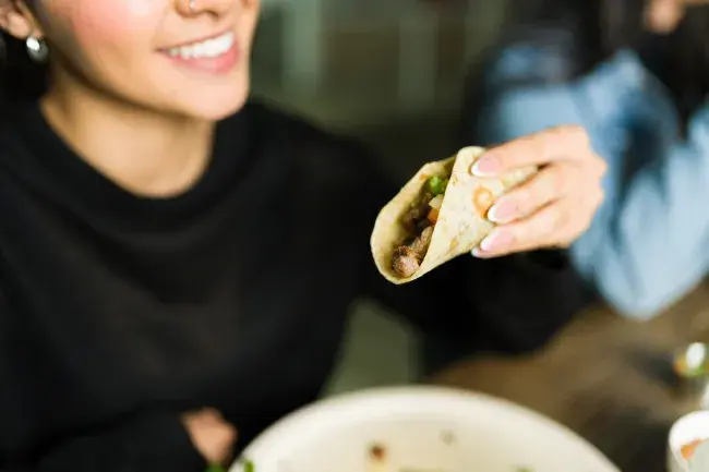 Person smiling while holding a chicken taco
