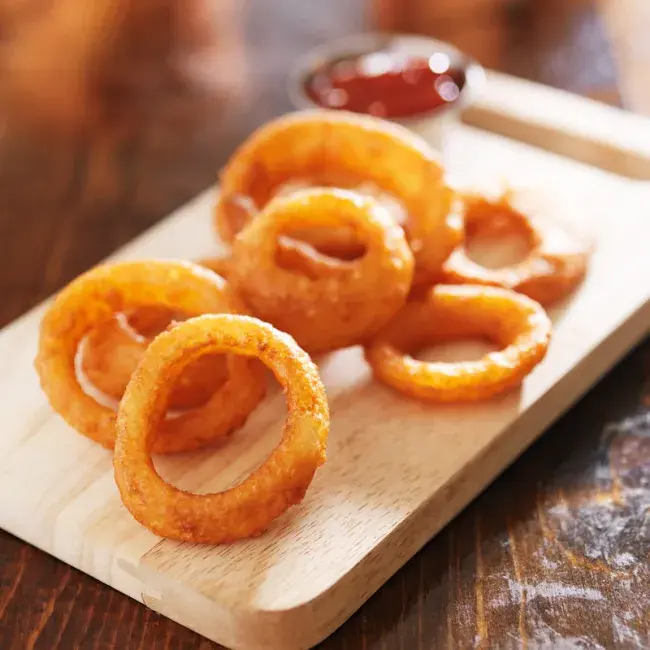 Crispy onion rings on a wooden board with dipping sauce