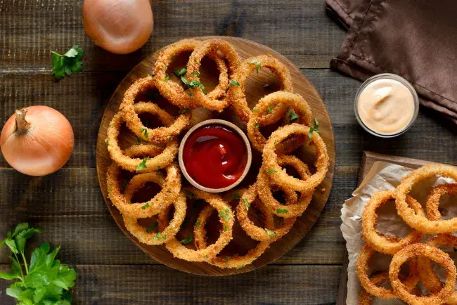 Crispy onion rings with dipping sauces on wooden table