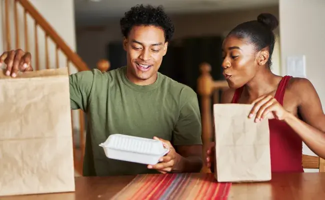 Couple opening takeout food bags at a table