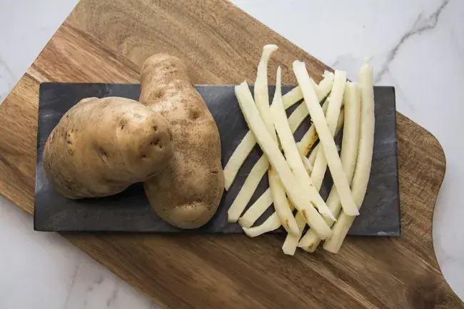 Whole russet potatoes with raw cut fries on a cutting board