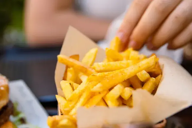 Hand grabbing a French fry from a basket of seasoned fries