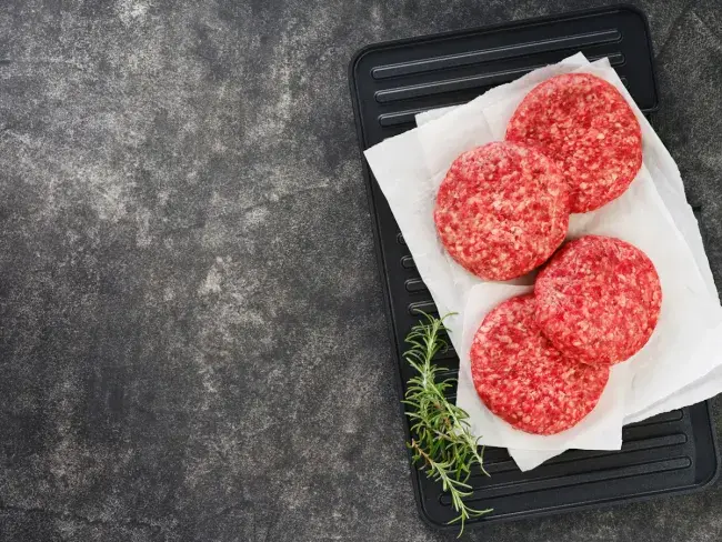 Raw burger patties on a tray with rosemary