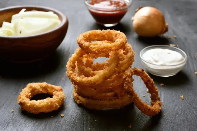 Stack of crispy onion rings with dipping sauces