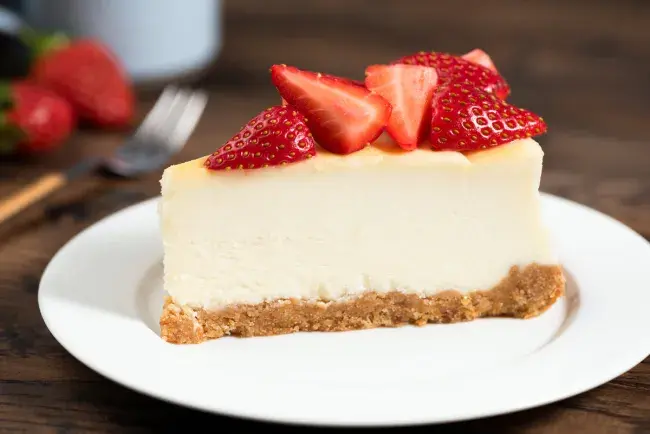 Slice of cheesecake on a plate topped with fresh strawberries