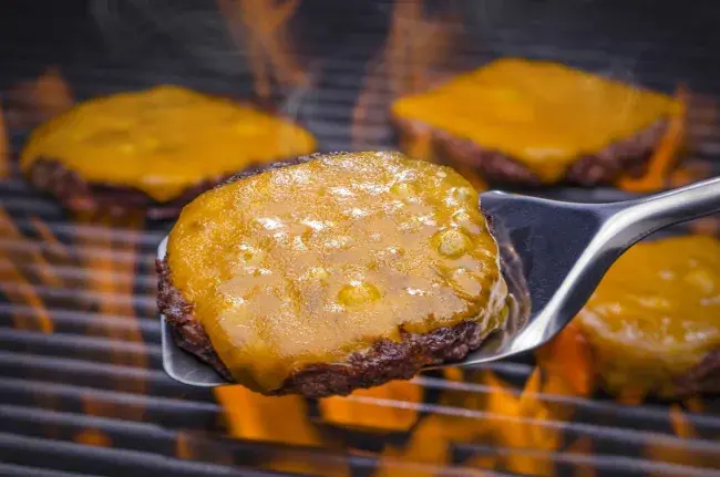 Grilled cheeseburger with melted cheese cooking over an open flame