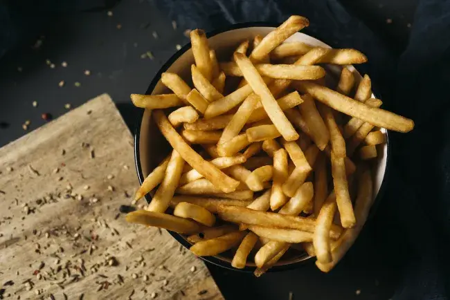 Golden, crispy French fries served in a bowl on a dark tabletop