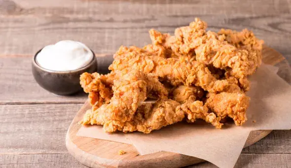 Golden fried chicken tenders on a wooden board with a side of dipping sauce