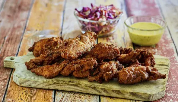 Crispy fried chicken tenders on a wooden board with coleslaw and dipping sauce