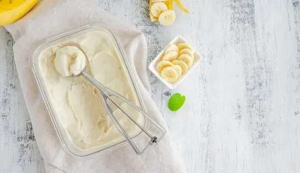 Banana custard in a glass dish with a scoop and sliced bananas on the side