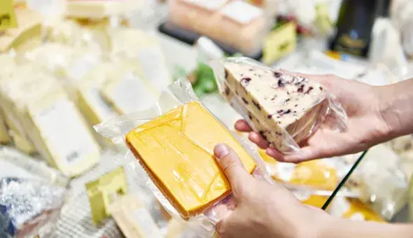 Person holding packaged cheese selections at a market display