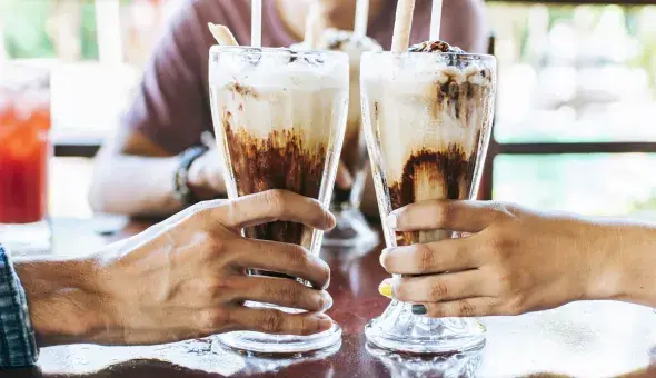 Two people clinking vanilla shakes with chocolate in tall glasses