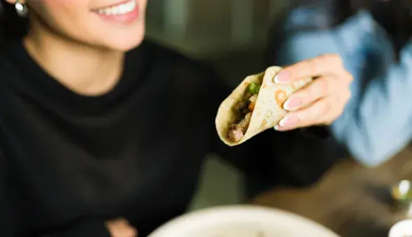 Person smiling while holding a chicken taco