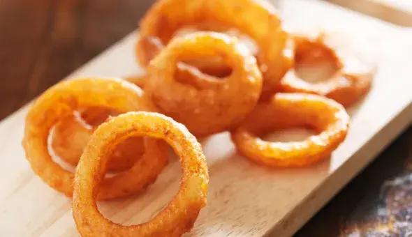 Crispy onion rings on a wooden board with dipping sauce