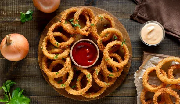 Crispy onion rings with dipping sauces on wooden table