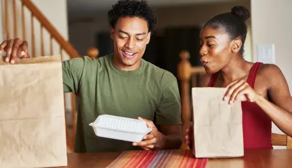 Couple opening takeout food bags at a table