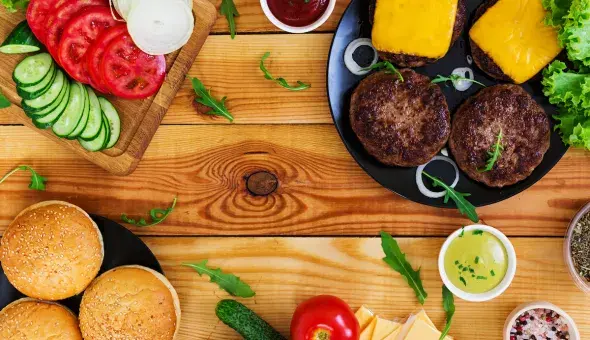 Burger ingredients and cooked patties with cheese on a wooden table