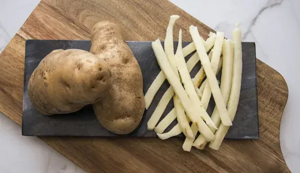 Whole russet potatoes with raw cut fries on a cutting board