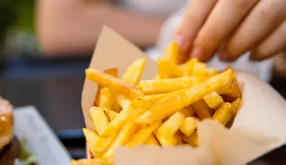 Hand grabbing a French fry from a basket of seasoned fries