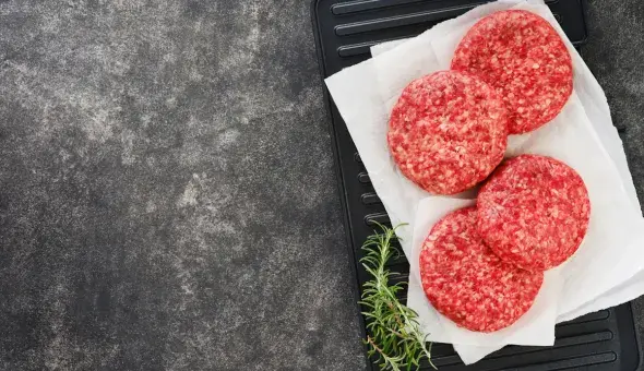 Raw burger patties on a tray with rosemary