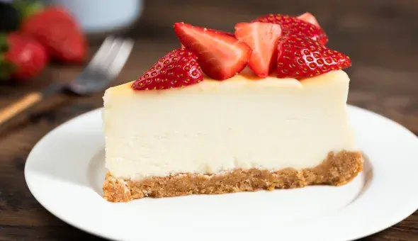 Slice of cheesecake on a plate topped with fresh strawberries