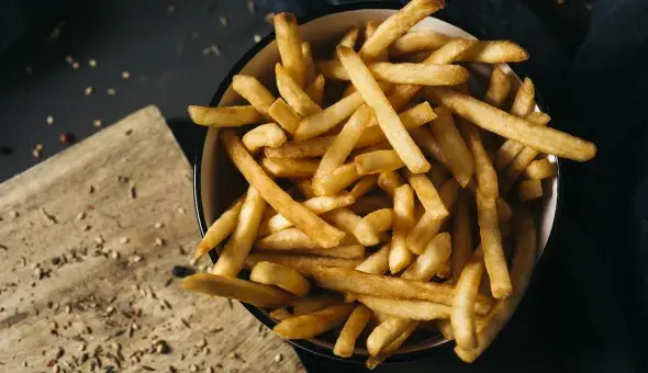 Golden, crispy French fries served in a bowl on a dark tabletop
