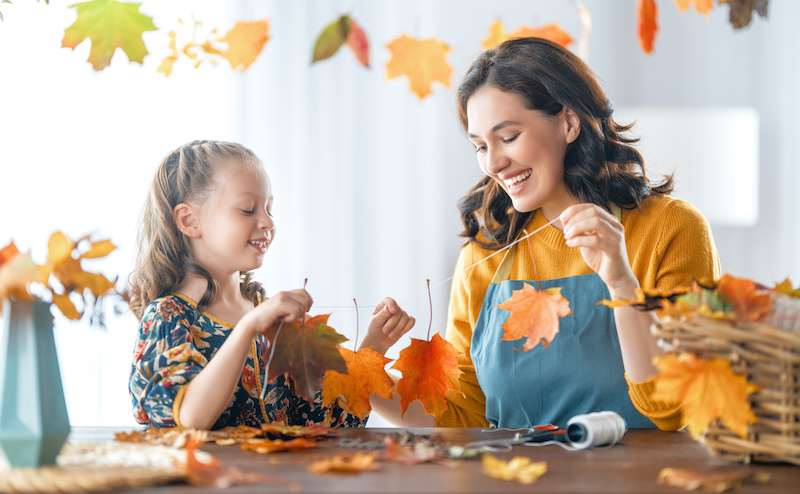 Mother and daughter making a fall leaf garland together at a table