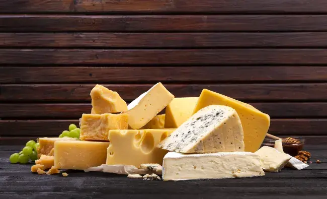 Assorted blocks and wedges of cheese on a dark wooden surface with grapes and nuts
