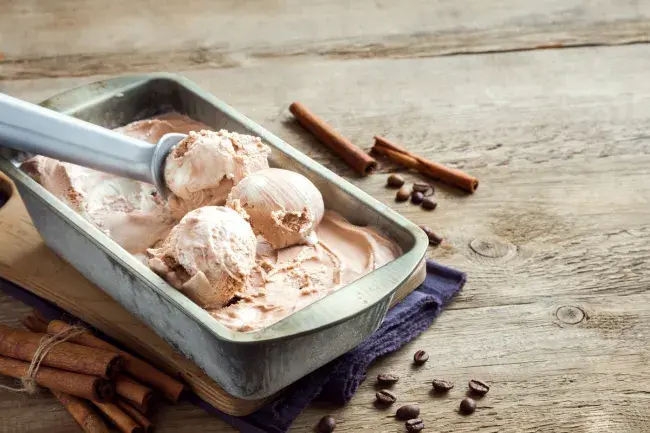 Ice cream in a metal pan with scoops and cinnamon sticks