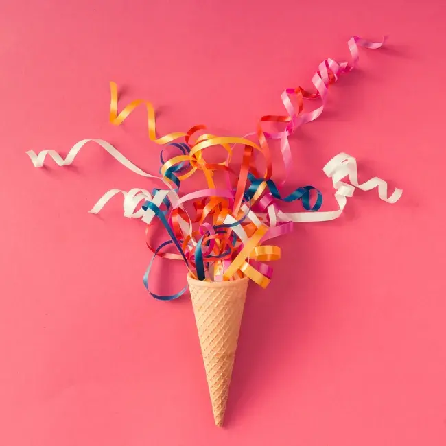 Ice cream cone filled with colorful curling ribbons on pink background
